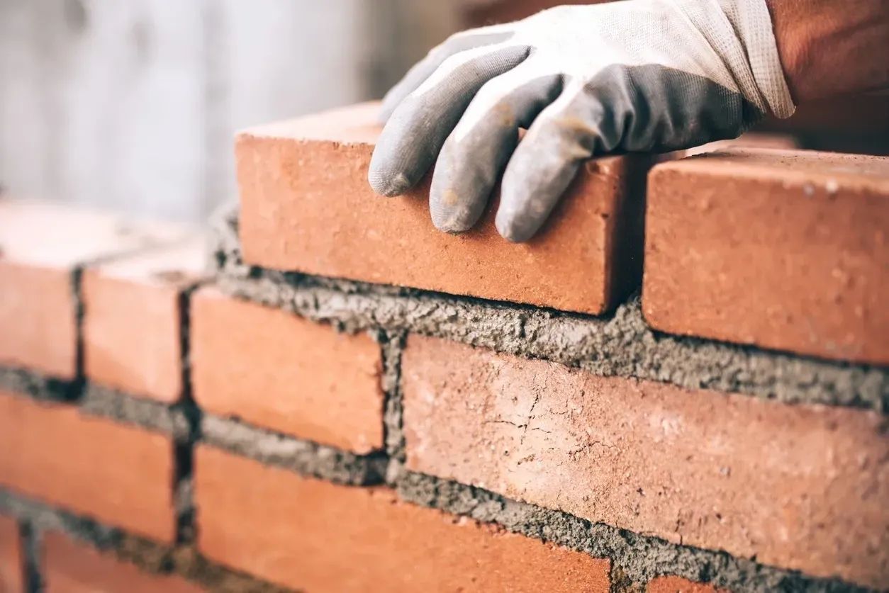 Gloved hand bedding a brick on a generous mortar bed