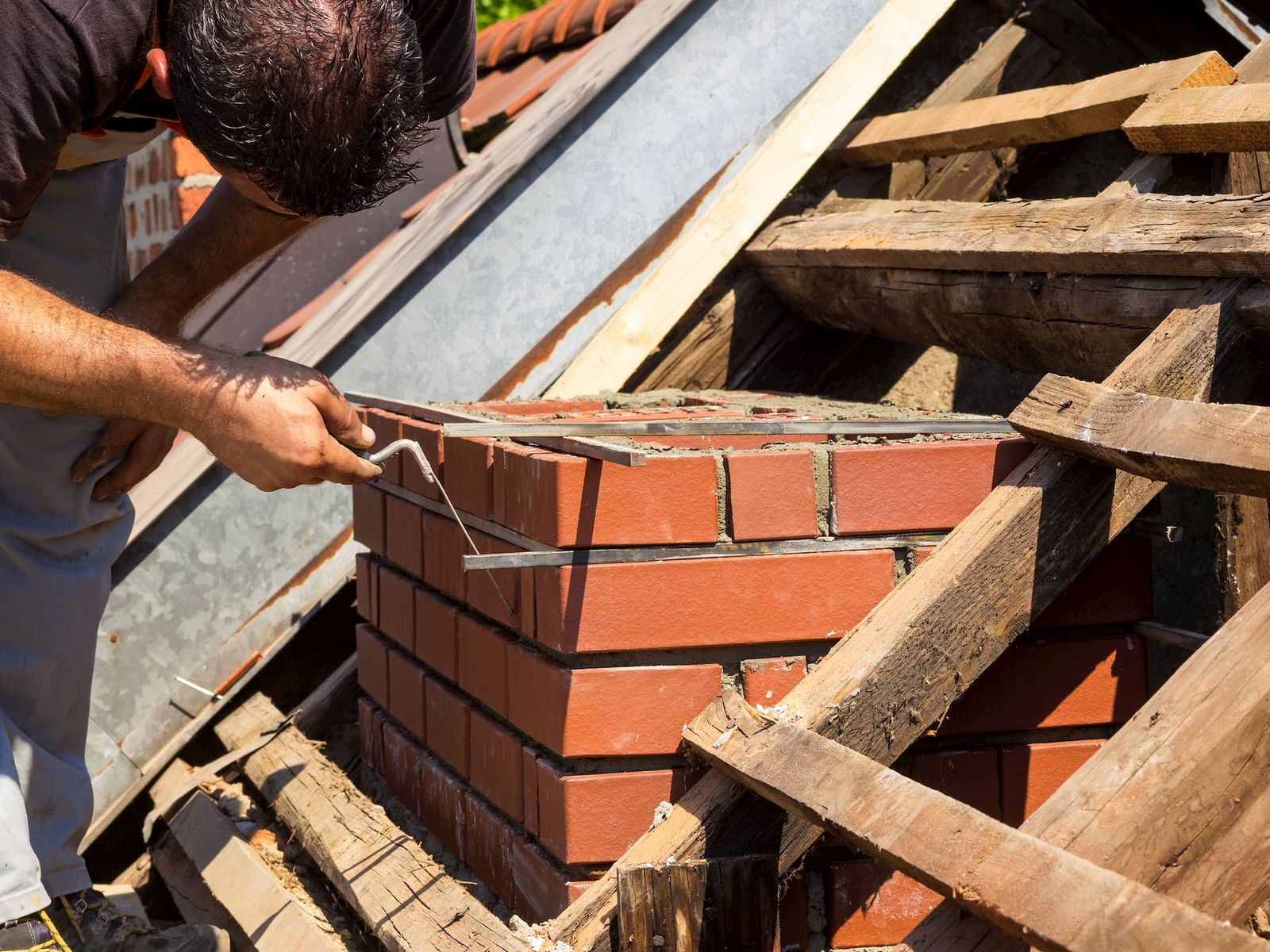 Mason truing a brick chimney rebuild among roof timbers